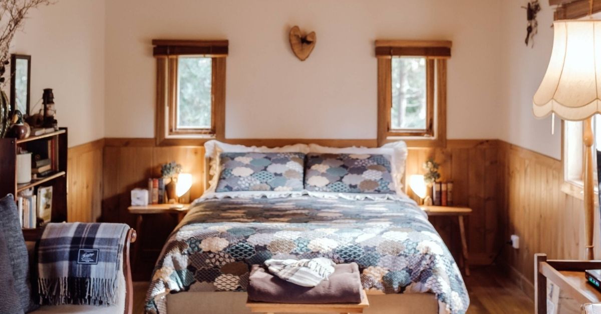 A double bed made up with a patterned quilt, with a bedside lamp and a framed picture above the headboard