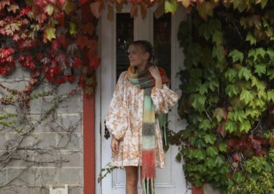 A woman in a patterned dress standing in a cottage doorway framed by red and green autumn ivy